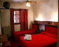 Habitaciones triples con cama matrimonial y otra simple decoradas en rojo y blanco con ventilador de techo de Hotel Valle del Sol