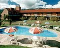 Parque con solarium con sombrillas y reposeras, piscina y al fondo del parque vista del hotel Valle del Sol